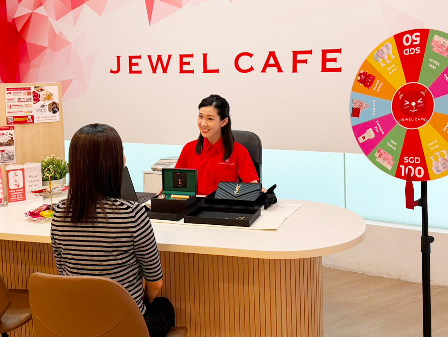 A Jewel Cafe staff member assists a customer with a jewelry appraisal at one of the brand